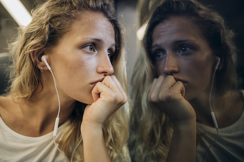 Woman with worried expression sitting on train looking out window, ruminating with worry about chronic disease