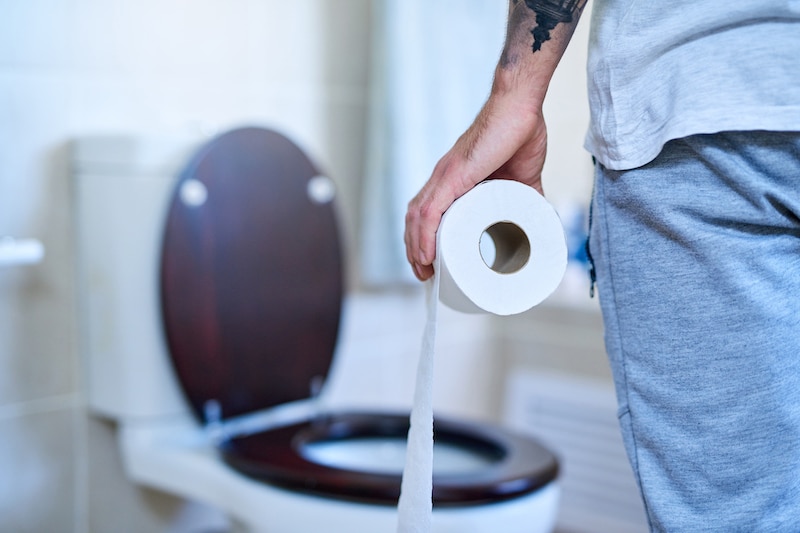 Common Crohn's symptoms; Man with roll of toilet paper enters bathroom