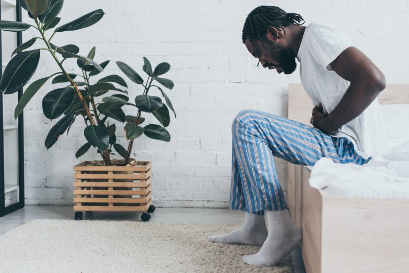Can you prevent Crohns flares; Man sitting on bed with abdominal pain